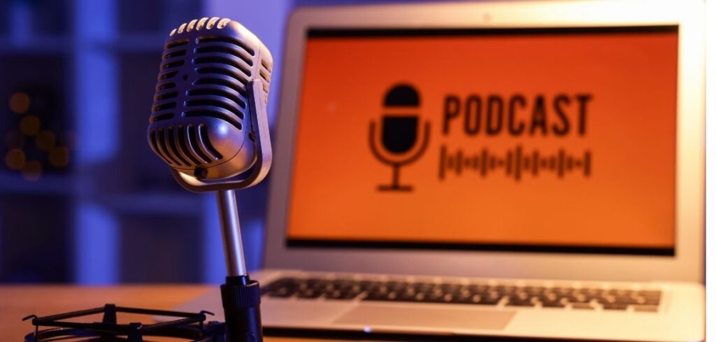 A desktop microphone positioned in front of a laptop displaying the word "Podcast," representing podcast recording or production