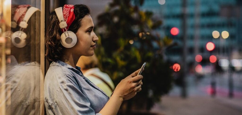 A person wearing headphones and using a smartphone outdoors, listening to audio or a podcast in an urban setting